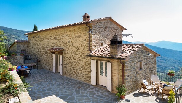 A stone building with a patio area, outdoor seating, and a view of the mountains. - Casale Pietrenta (Cortona)