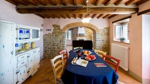 A dining area with a table set for four, stone walls, wooden beams, and a window with a plant. - Casale Pietrenta (Cortona)