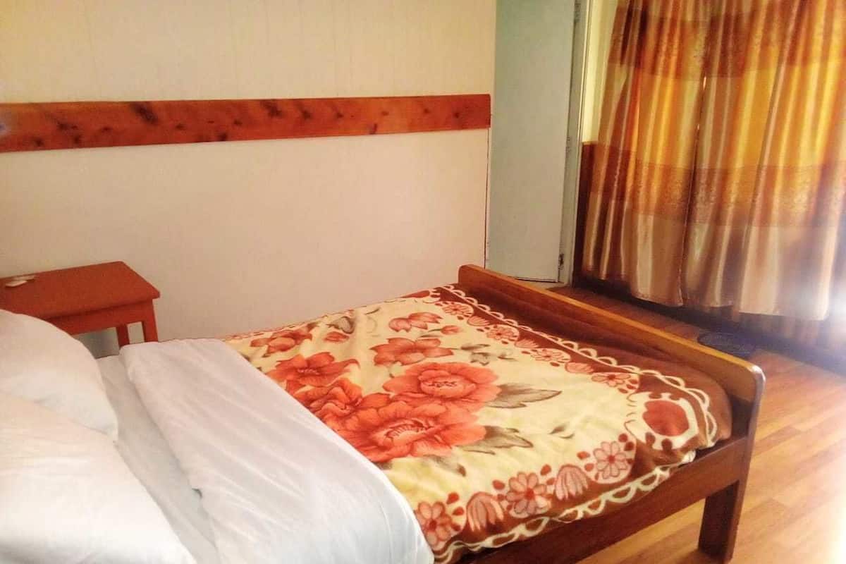 Una cama con colcha estampada, cabecero de madera y una mesita de noche pequeña.