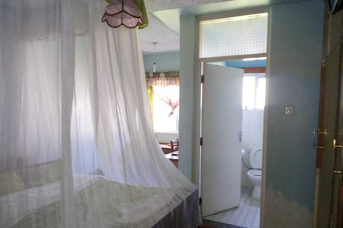 Un dormitorio con cama a dosel, un baño visible con inodoro, y una puerta que da a otra habitación.