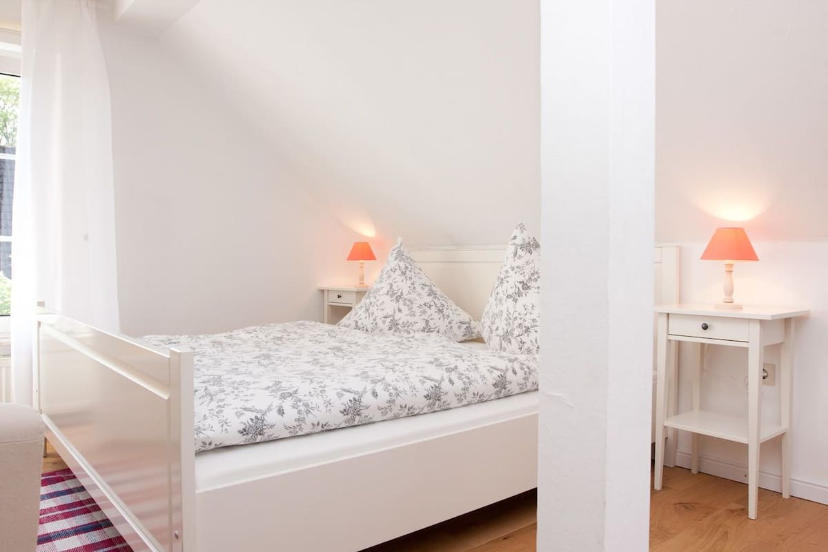 A white bedroom with a single bed, two bedside lamps, and a nightstand.