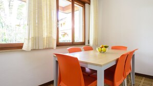 Ein Essbereich mit Tisch und orangefarbenen Stühlen, eine Obstschale auf dem Tisch und ein Fenster mit Vorhängen.