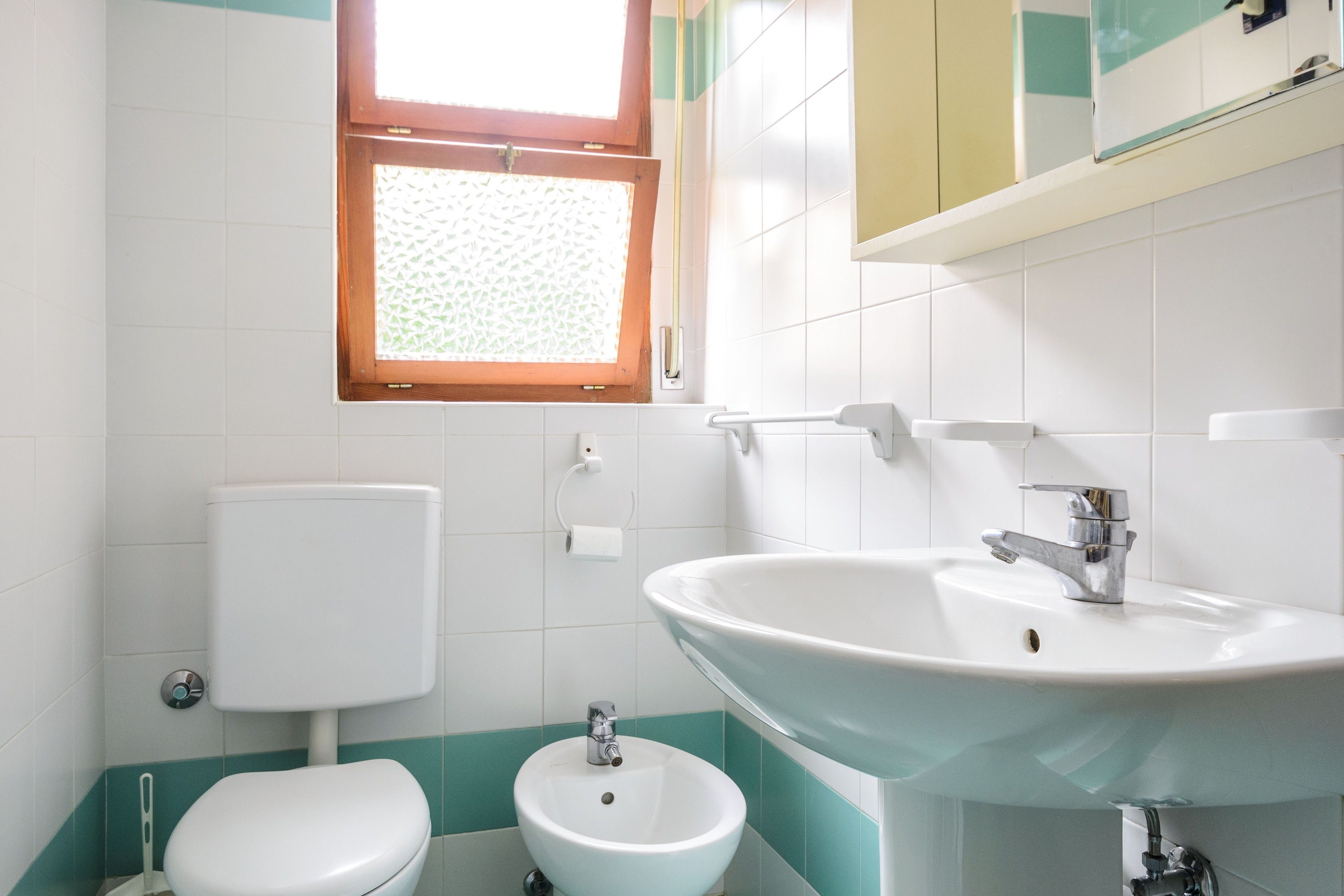 A bathroom with a toilet, bidet, sink, and a window.