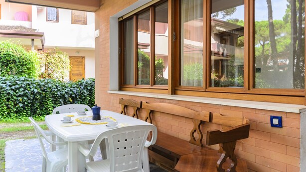 Eine Terrasse mit Tisch und Stühlen, einer hölzernen Bank und einem Fenster mit Blick ins Grüne.