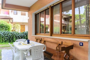 A patio with a table and chairs, a wooden bench, and a window with a view of greenery.