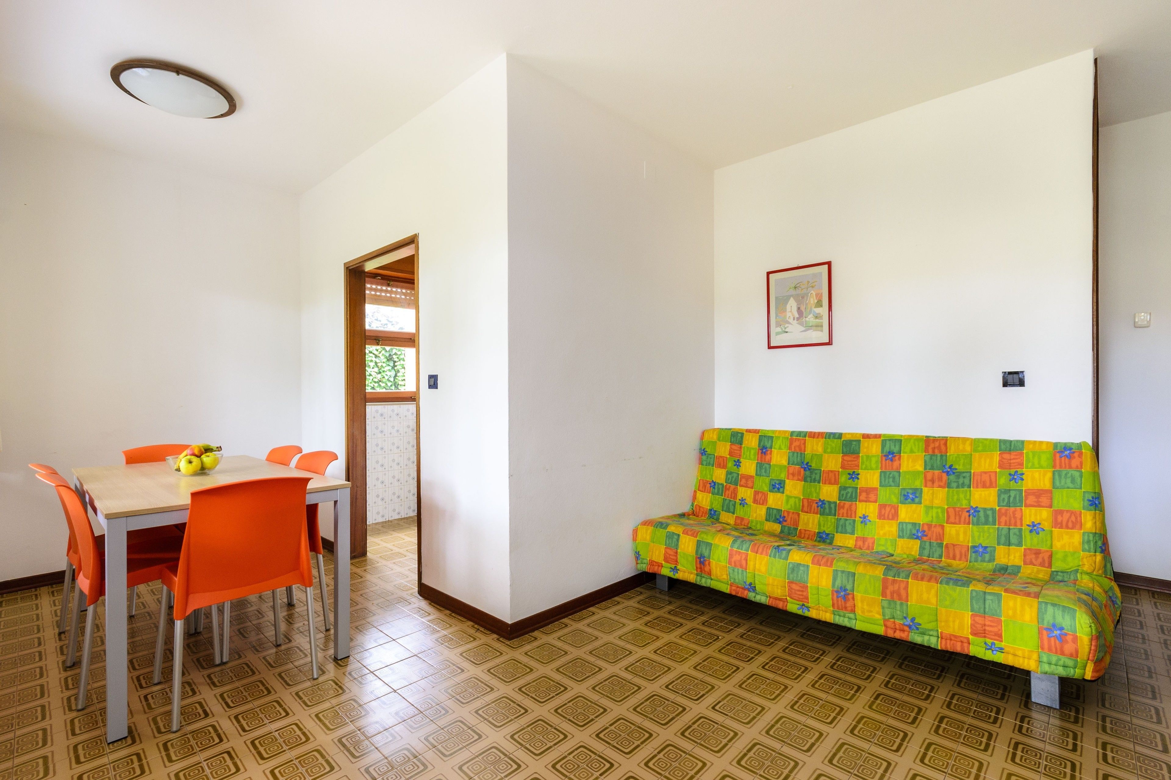 Una habitación con una mesa de comedor y sillas, un sofá colorido y un suelo estampado.