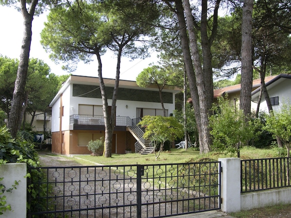 A two-story building with a balcony, surrounded by trees and a gated entrance.