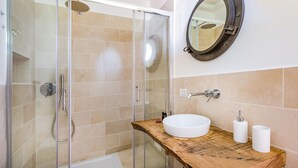 A modern bathroom with a glass-enclosed shower, a wooden vanity with a white sink, and a round mirror with a ship's porthole design. - Doneduà (Vico Equense)