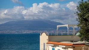 A coastal view with a mountain in the background, a body of water in the foreground, and a building with a balcony. - Doneduà (Vico Equense)
