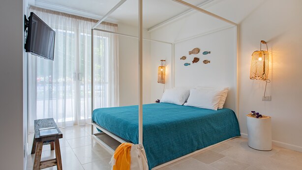 A bedroom with a four-poster bed, a television on the wall, and a small stool. - Doneduà (Vico Equense)