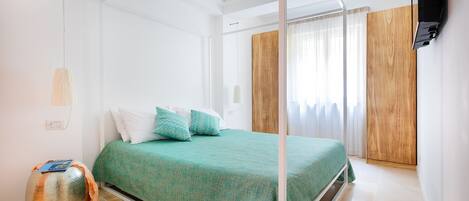 Un dormitorio con cama, un armario de madera, un televisor y una mesa redonda con un libro.