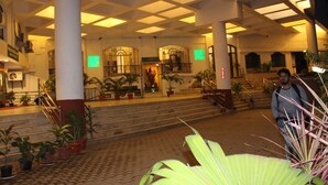 A spacious lobby with a high ceiling, multiple staircases, and potted plants. - Hotel Pooja International (Davanagere)