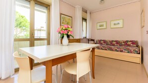 Un comedor con una mesa y sillas blancas, un sofá con un cojín floral y un jarrón de flores rosas.
