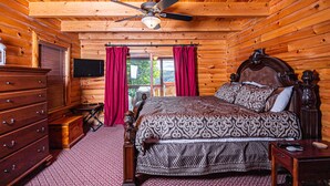 Een slaapkamer in een blokhut met houten plafond, een bed met beddengoed met dessin, een dressoir en een televisie aan de muur.