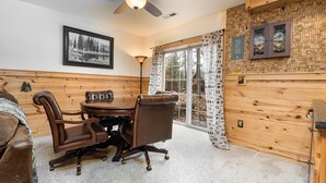 Una habitación con pared de madera, un ventilador de techo, una mesa de comedor con sillas y una ventana con cortinas.