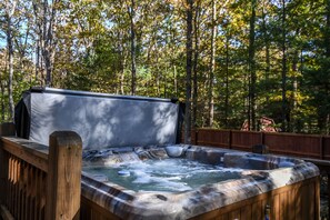 A hot tub in a wooded area with a wooden deck and a covered section.