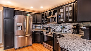 A modern kitchen with dark cabinetry, stainless steel appliances, and a granite countertop. - Castle in the Sky 5 Bedroom House (McHenry)