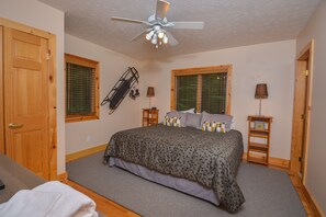A bedroom with a bed, a ceiling fan, wooden doors, and a window with blinds. - Hootenanny 5 Bedroom House (McHenry)