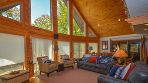 A spacious living room with large windows, wooden ceiling, and comfortable seating.
