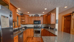 A kitchen with wooden cabinets, a stainless steel refrigerator, a granite countertop, and a microwave.