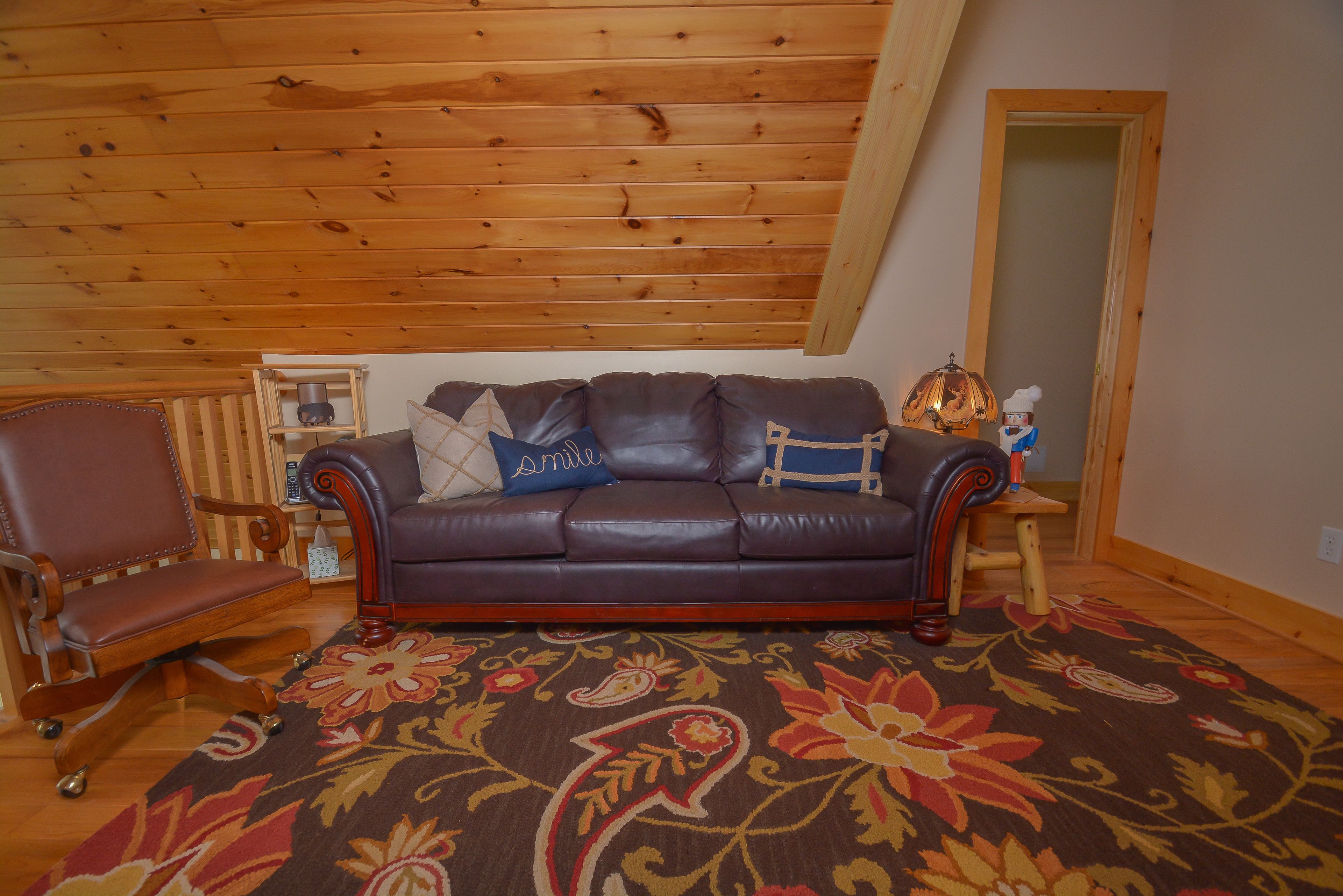 A room with a brown leather sofa, a wooden chair, and a patterned rug.