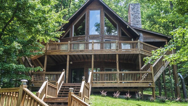 A wooden cabin with a balcony and a stone chimney, surrounded by trees.