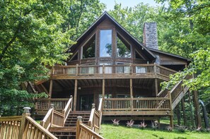 A wooden cabin with a balcony and a stone chimney, surrounded by trees. - Hootenanny 5 Bedroom House (McHenry)