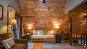 Ein gemütliches Zimmer mit Holzbalkendecke, einer Couch mit Kissen, einer Holzbank und zwei Lampen.
