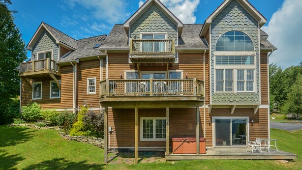 A large, multi-story wooden house with a balcony, a garage, and a patio area. - Green Gables 4 Bedroom House (McHenry)