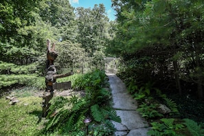 Un sendero de piedra que atraviesa un jardín exuberante con helechos y un letrero de madera que dice “BIENVENIDOS”.