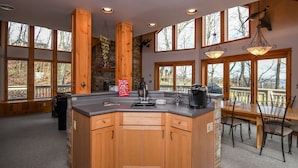 A spacious kitchen with wooden cabinets, a large island, and a dining area with chairs. - Bluebird Daze 4 Bedroom House (McHenry)