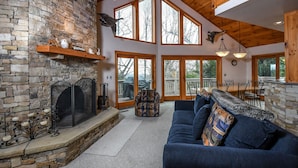 A cozy living room with a stone fireplace, a blue sofa, and a dining area with a stone bar. - Bluebird Daze 4 Bedroom House (McHenry)