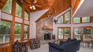 A spacious living room with a stone fireplace, large windows, and wooden beams. - Bluebird Daze 4 Bedroom House (McHenry)