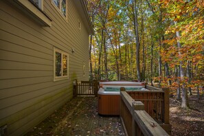 Eine Holzterrasse mit Whirlpool, umgeben von Bäumen mit Herbstlaub.
