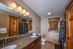 Ein Badezimmer mit Granitplatte, zwei Waschbecken, einem großen Spiegel und einer Dusche mit Fenster.