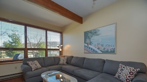 Ein Wohnzimmer mit einem grauen Ecksofa, einem Glastisch und einem roten Teppich mit Muster.