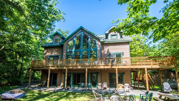 A two-story wooden house with a balcony, surrounded by trees.