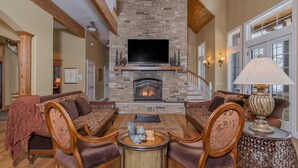 A spacious living room with a stone fireplace, comfortable seating, and a television.
