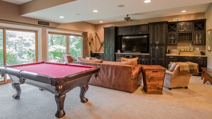 A pool table in a well-lit room with dark cabinets and a large flat-screen TV. - Canadian Day 4 Bedroom House (McHenry)