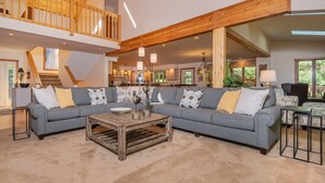 Un vaste espace de vie comprenant un grand canapé d’angle gris, une table basse en bois et un escalier menant à un niveau supérieur.