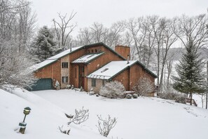 A wooden cabin with a green roof, surrounded by snow-covered trees and a snowy landscape.