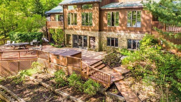 Une maison en bois à deux étages, dotée d’une terrasse, d’un espace salon extérieur et de fondations en pierre.