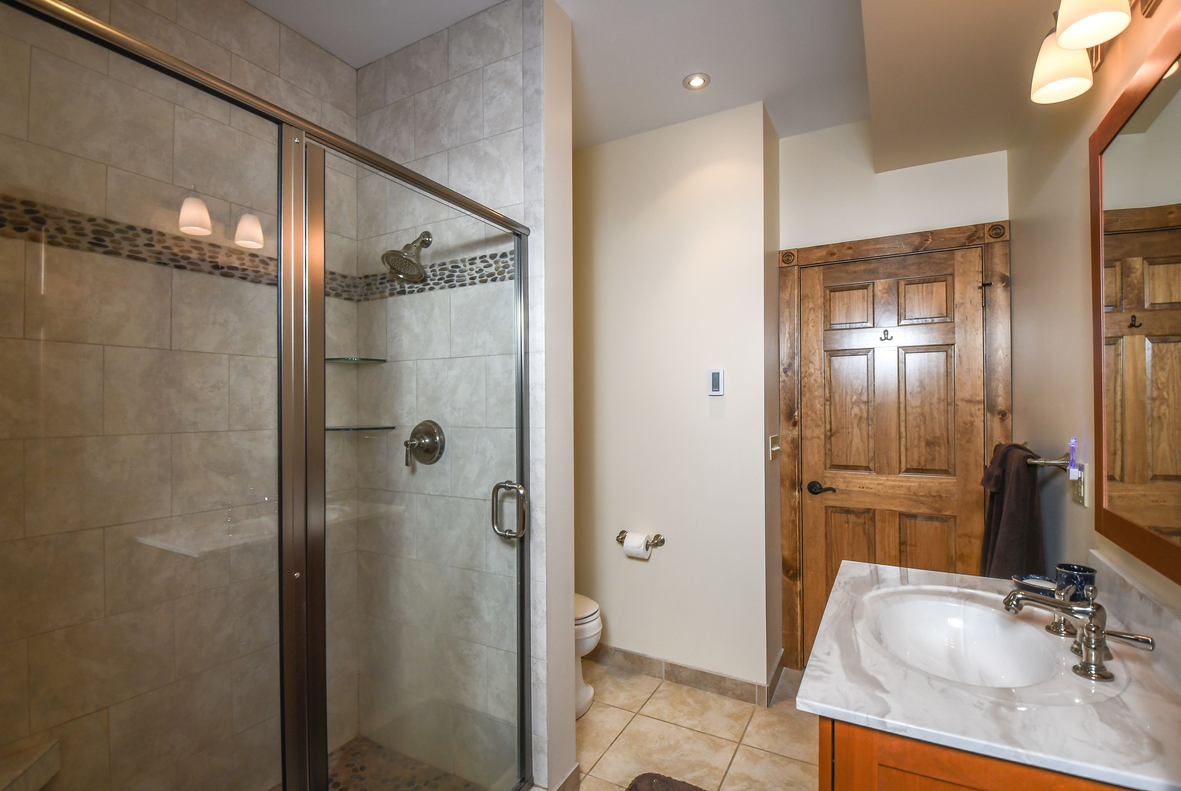 A bathroom with a glass-enclosed shower, a wooden door, and a white sink with a mirror above it.