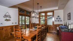 A wooden dining table with chairs, a chandelier, and a "Welcome to the Lake" sign on the wall.