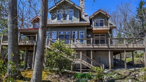A large, multi-story house with a prominent balcony and a stone chimney.