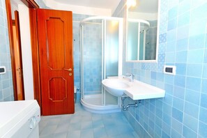 Um banheiro com porta de madeira, box de vidro, pia branca e paredes com azulejos azuis.
