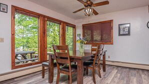 A dining area with a wooden table and chairs, large windows with wooden frames, and a ceiling fan. - Lake View 3 Bedroom House (Oakland)