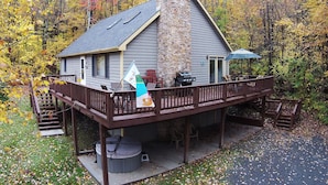 A house with a stone chimney, a deck with outdoor furniture, and a flag. - Home Sweet Cabin 4 Bedroom House (Oakland)