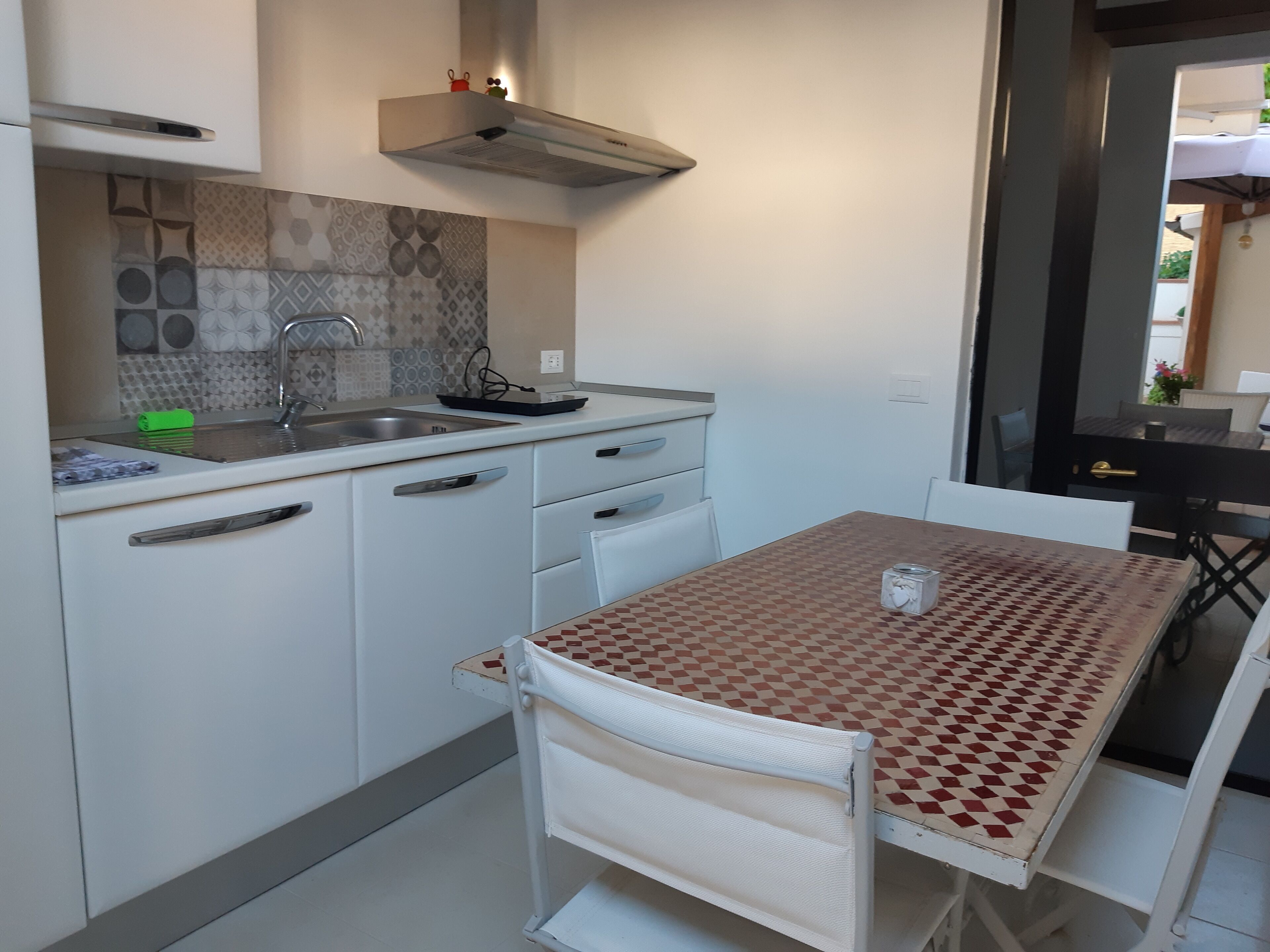 Een kleine keuken met een spoelbak, een kookplaat en een eethoek met een geruit tafel en stoelen.