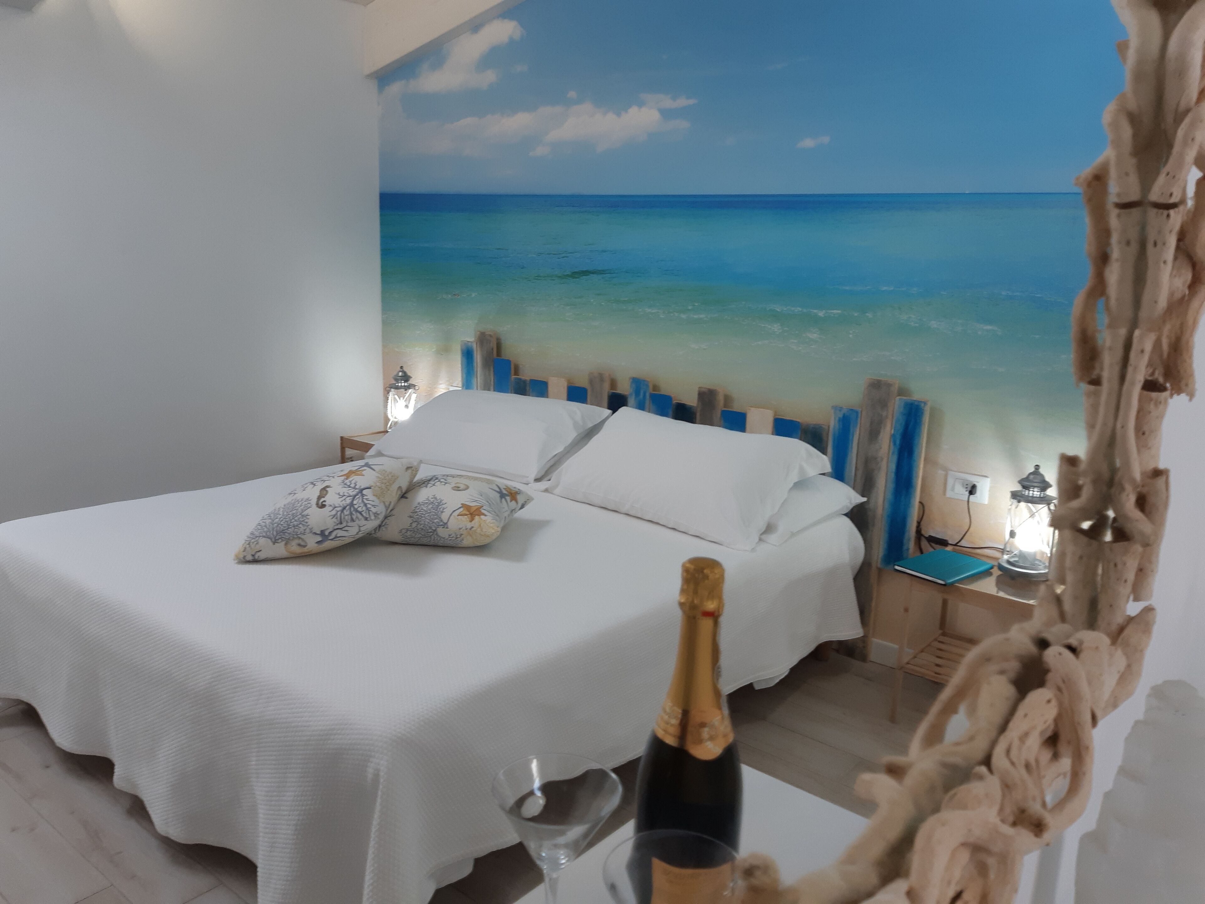 A bedroom with a bed, pillows, a bottle of champagne, and a glass.